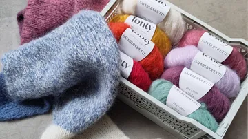Colorful yarn balls in basket beside knitted fabric.