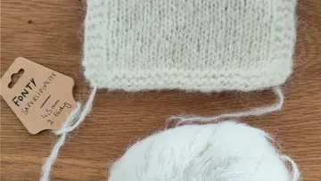 Knitted swatch beside yarn ball on table.