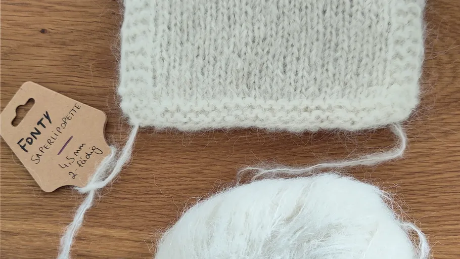 Gestricktes Muster neben Wollknäuel auf Tisch.