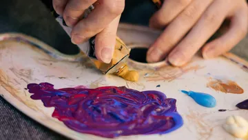 Hand drückt Farbe auf Künstlerpalette.