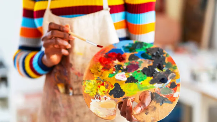 Person holding paint palette and brush indoors.