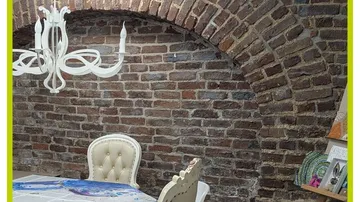 Esstisch und Kronleuchter in Backsteinraum.