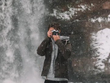 Junger Mann fotografiert vor einem Wasserfall im Schnee.