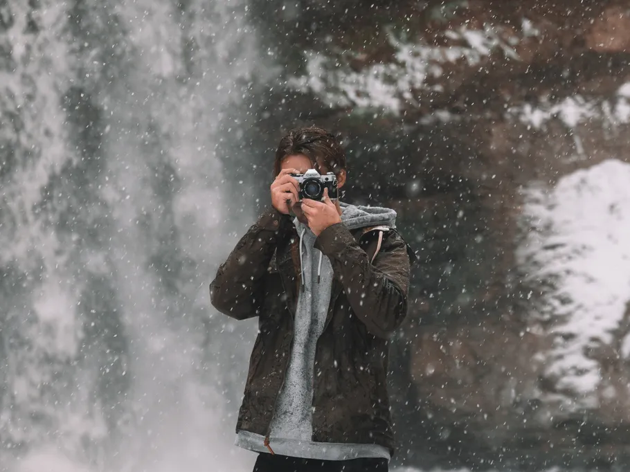 Junger Mann fotografiert vor einem Wasserfall im Schnee.