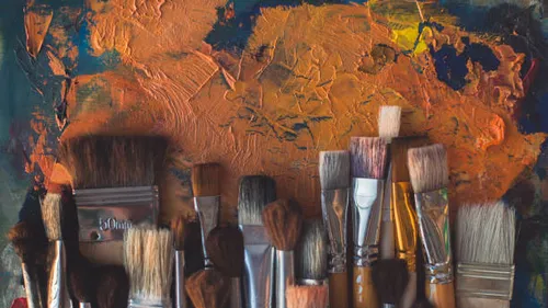 Paintbrushes resting against colorful, textured canvas.