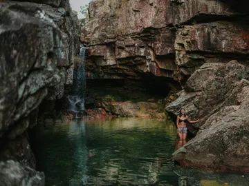 Frau steht im Wasser zwischen hohen Felsen und Wasserfall.