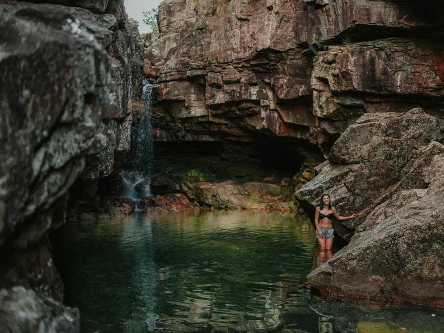 Woman standing in water between high rocks and waterfall.