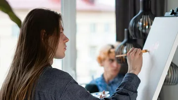 Person malt auf Staffelei drinnen, fokussierter Ausdruck.