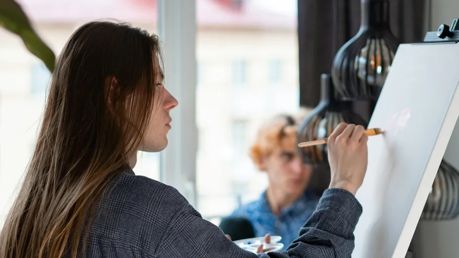 Person painting on easel indoors, focused expression.