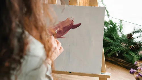 Person painting on canvas with plants nearby.