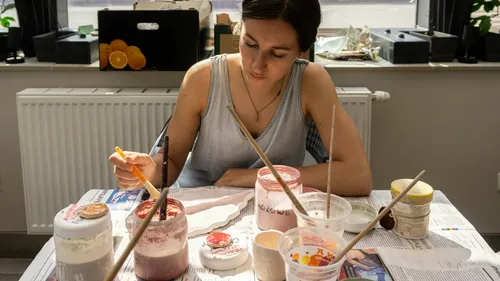 Woman painting pottery at a table indoors.