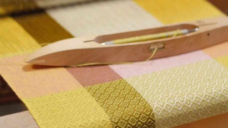 Wooden shuttle on colorful woven fabric.