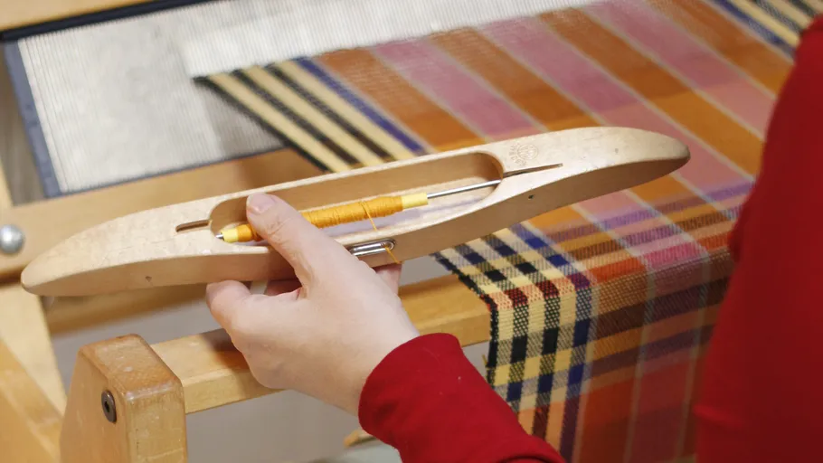 Hand holding shuttle on wooden loom.