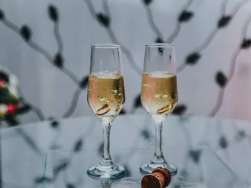 There are two champagne glasses on a table with corks next to them.