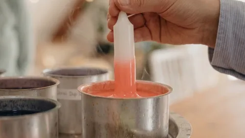 Hand dipping candle into colored wax.