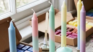 Bunte Kerzen auf Holztisch am Fenster.