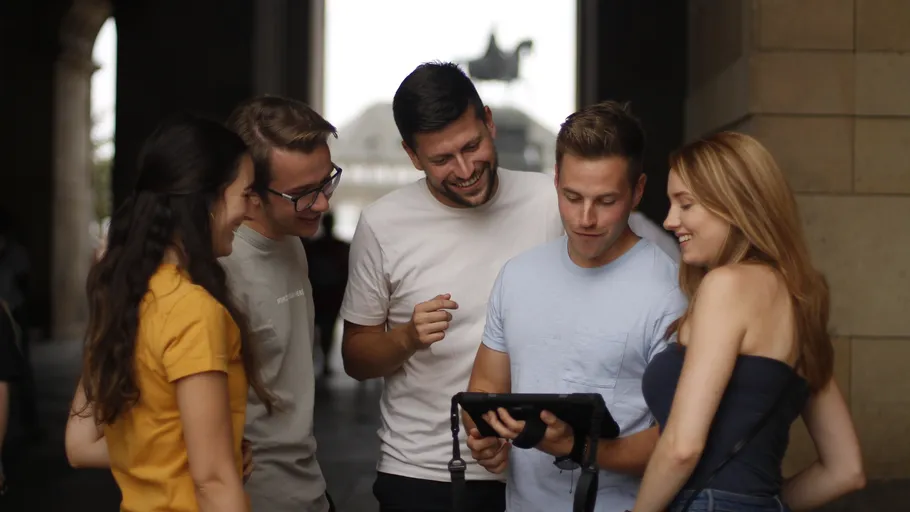 Group of five people smiling at tablet outside.