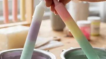 Hand taucht bunte Kerze in Wachstopf.