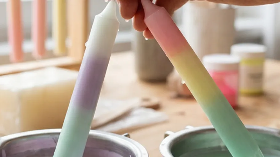 Hand dipping colorful candle in wax pot.