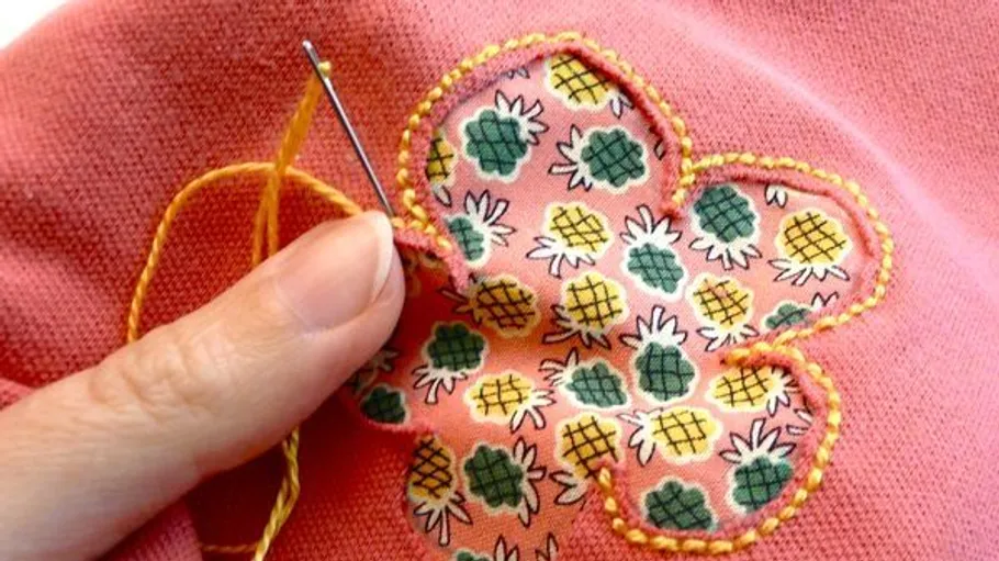 Hand stitching a patch on pink fabric.