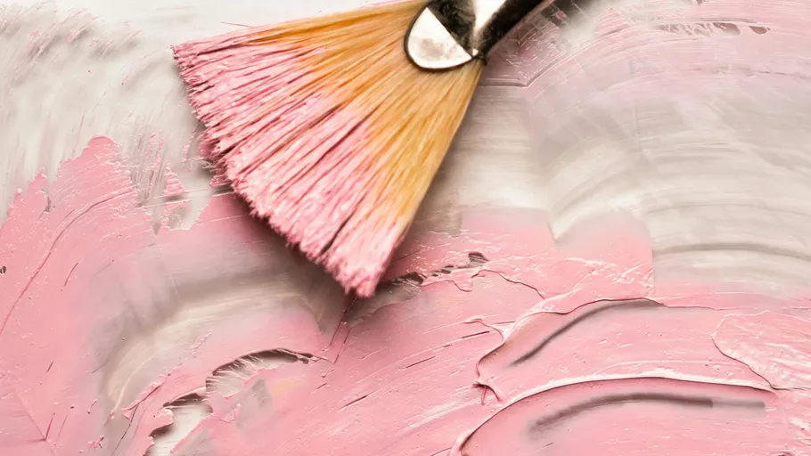 Paintbrush applying pink paint on a canvas.