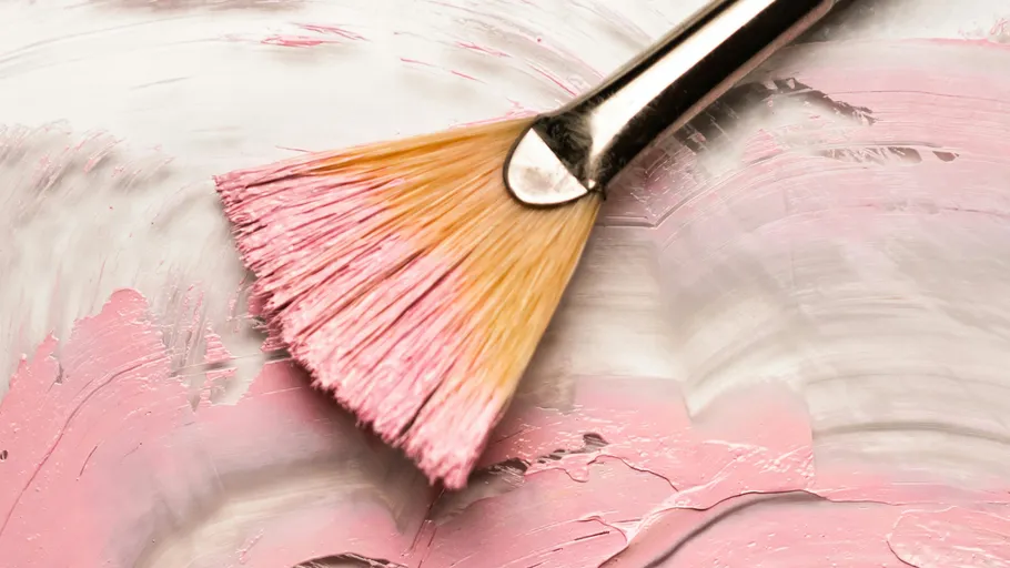 Paintbrush applying pink paint on canvas.