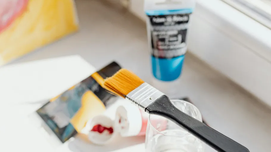 Paintbrush dipping in glass near art supplies.