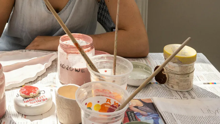 Person painting with jars on newspaper-covered table.