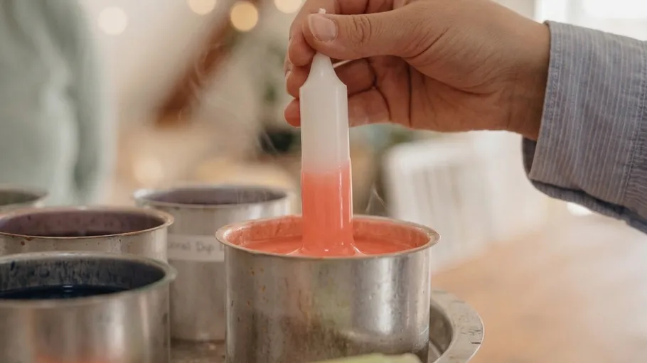 Hand dipping candle into colored wax.