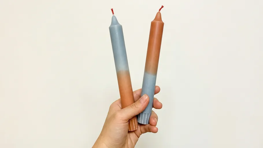Hand hält zwei farbige Kerzen, weißer Hintergrund.