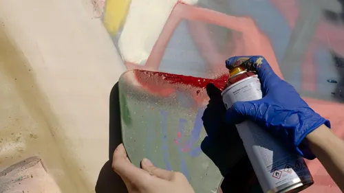 Hand sprüht Graffiti auf bunte Wand.