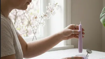 Person holding a candle near a window.