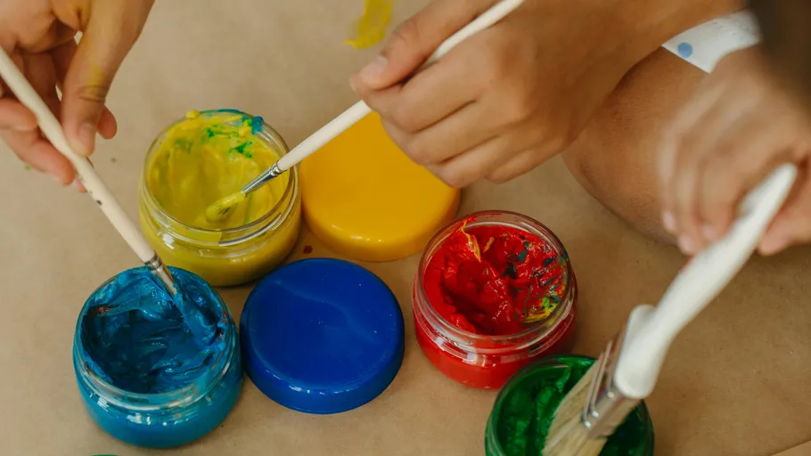 Hands dip brushes into colorful paint jars.