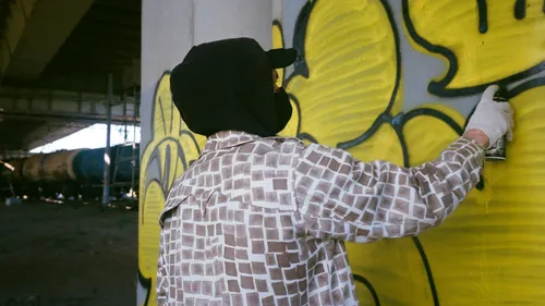Person spray-painting yellow graffiti under bridge.