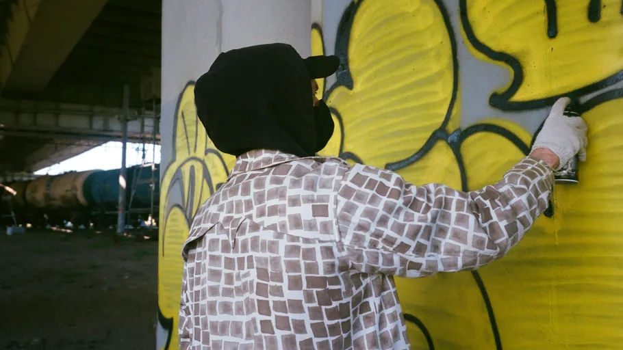 Person spray-painting yellow graffiti under bridge.