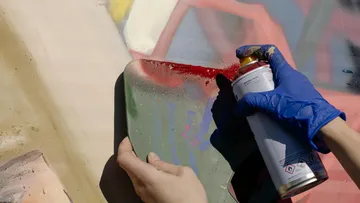 Behandschuhte Hände sprayen Wand mit Schablone.