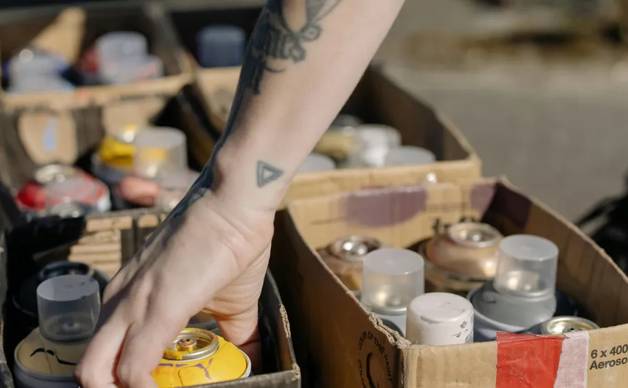Tätowierte Hand wählt Spraydosen.