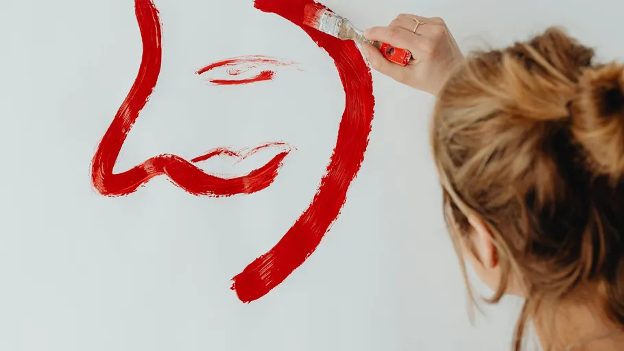 Woman painting red face on white canvas.