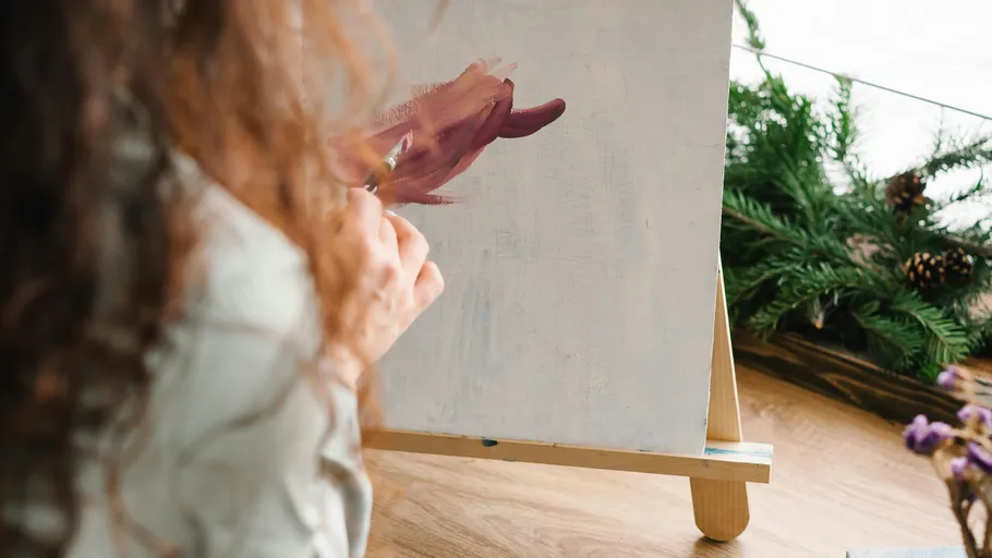 Person painting on canvas with easel indoors.
