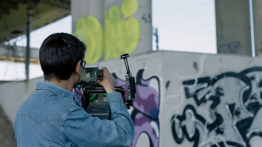 Person filming graffiti under a bridge.
