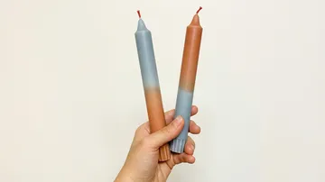 Hand holding two gradient candles vertically.