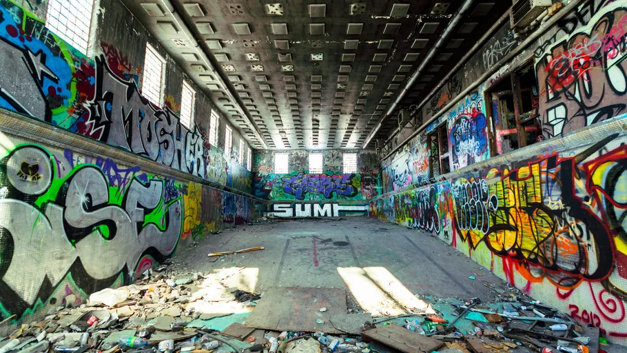 Abandoned graffiti-covered indoor pool, debris scattered.