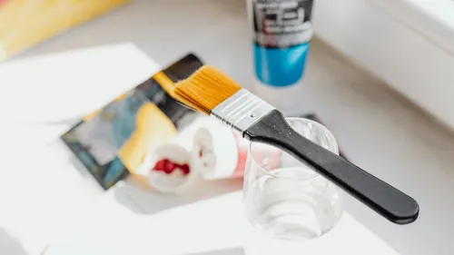 Paintbrush resting on glass, art supplies nearby.