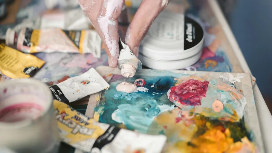 Hand drückt Farbe auf eine bunte Palette.