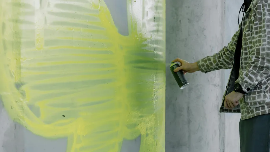 Person spray paints yellow graffiti on wall.