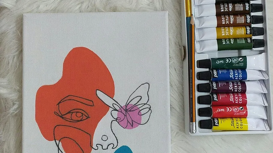 Colorful abstract face sketch beside paint tubes.