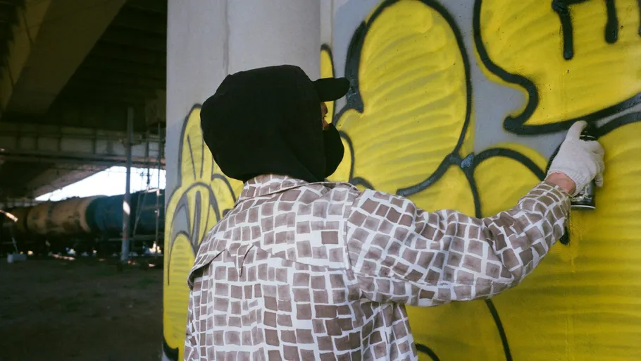 Person spray painting graffiti on concrete pillar.