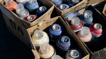 Spray paint cans in cardboard boxes outdoors.