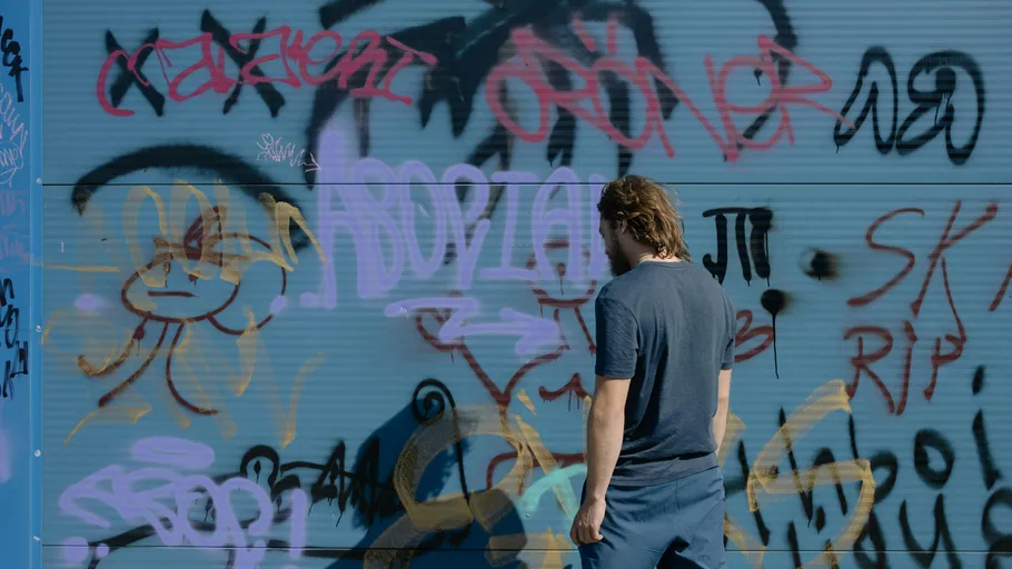 Mann steht vor graffiti-bedeckter Wand im Freien.