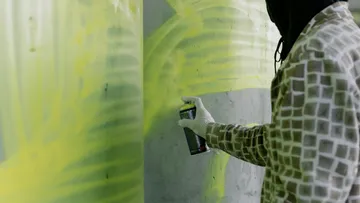 Person sprüht Farbe auf Betonwand.